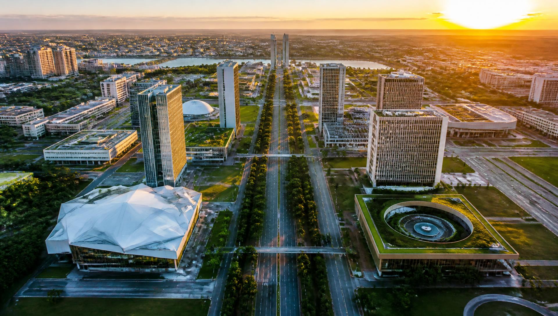 Vista aérea de uma cidade brasileira moderna ao pôr do sol, com grandes avenidas arborizadas e arquitetura contemporânea
